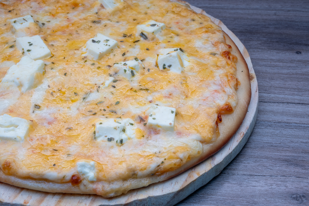 A close-up of a cheese pizza topped with cubes of feta on a wooden board.